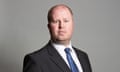 head and shoulders portrait against grey background: Rob Roberts is youngish with a round face and gingery close-cropped beard and hair, and wears a dark suit and blue tie