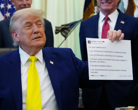 Man in bright yellow tie at desk, surrounded by smiling men, holds up piece of paper.