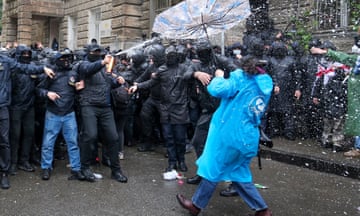 Police aim a spray at a person carrying an umbrella.