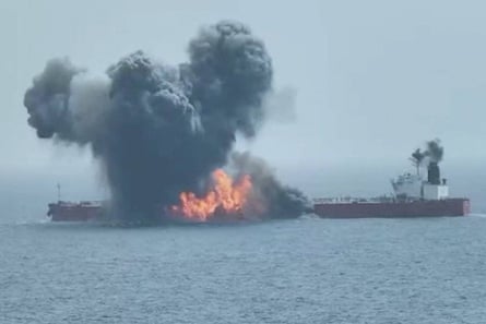 An aerial view of smoke and flames billowing from an oil tanker as another cargo ship sits nearby