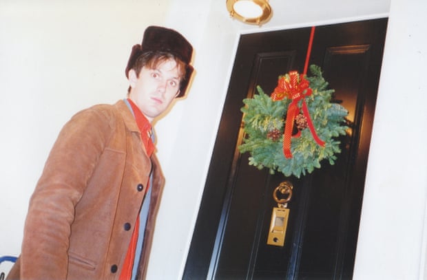 A younger Dave McCormack, in New York posing next to a door with a Christmas wreath, wearing a surprised expression