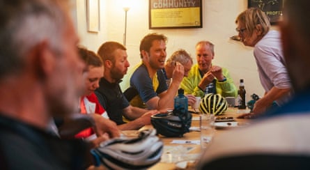 A group of cyclists sitting round a hostel table eating and talking.