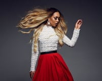Rebecca Ferguson poses with flowing hair in a lace top and red skirt