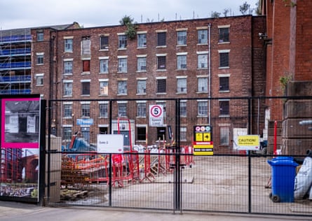 A locked gate with warning signs fronts Weir Mill, a brick building under renovation in Stockport.