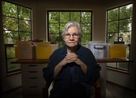 woman seated in front of file boxes and windows with green trees behind them. her hands are folded
