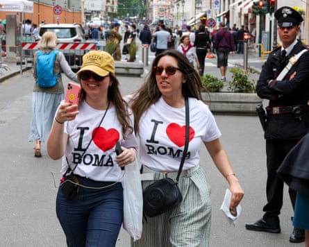 Two women wearing I Heart Roma T-shirts walk along a Roman street taking a selfie