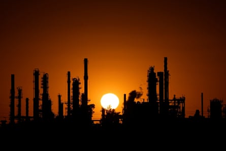 the sun sets behind an oil refinery