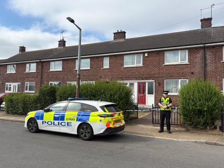 Police officer on a pavement alongside a parked police car, in front of terrace houses