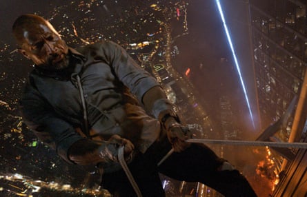 Dwayne Johnson leans back holding a rope in each and with a cityscape at night far below