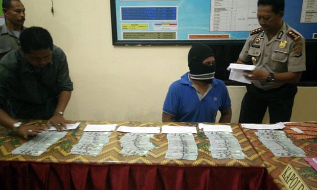 A masked Indonesian crew member of an alleged people-smuggling boat is put on display behind a table of US dollar notes at a press conference on Rote Island in June.