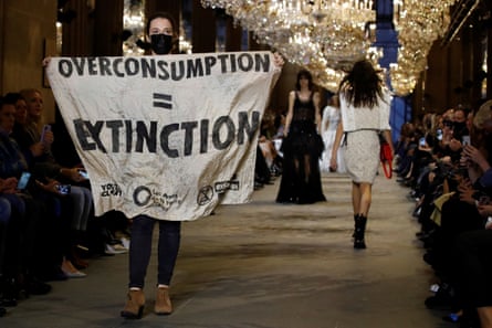 An activist with a banner that says “Overconsumption = Extinction” gatecrashes a show at Paris fashion week in 2021.