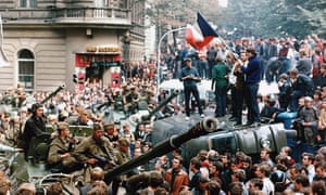 Czech youngsters holding a Czechoslovak flag stand atop an overturned truck as other Prague residents surround Soviet tanks in Prague, 21 August 1968.