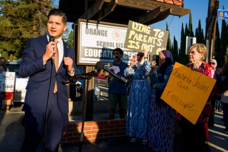 A man speaks into a microphone in front of a crowd of people holding protest signs.