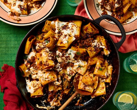 Turkish lamb and hot pepper paccheri in a pan with a wooden spoon, and served on three plates next to the pan, all placed on a green cloth with napkins and glasses of water.