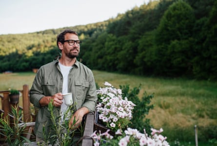 Hygge moment for handsome barefoot man, standing outdoor on patio and drinking warm herbal tea.