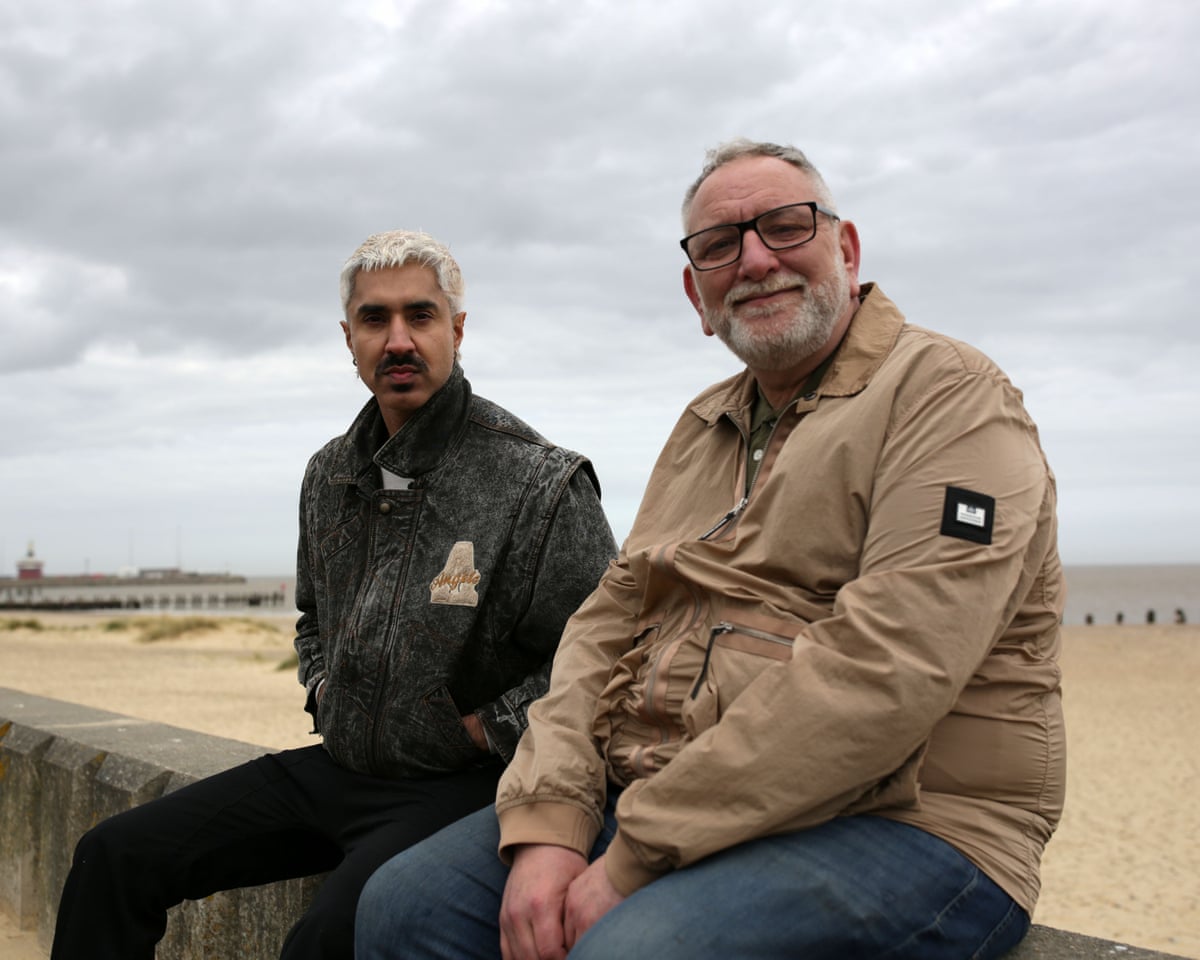 Azhar and Ivan sit together on a stone wall beside a sandy beach