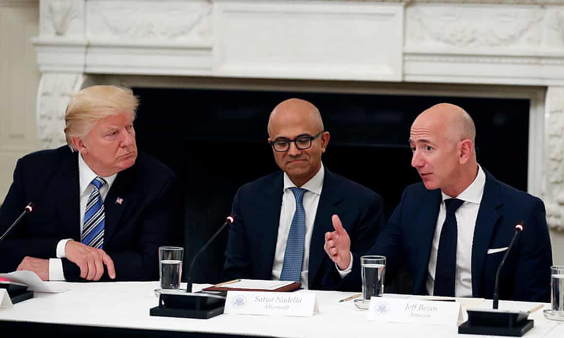 Donald Trump and Satya Nadella listen while seated together at a table as Jeff Bezos speaks