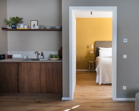 A small kitchenette and a view through an open door into a bedroom with yellow painted walls.