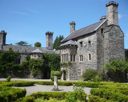 The three-storey fortified Tudor manor house, built of grey stone, with large chimneys, small windows and an ornate garden laid out in front