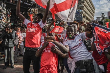 Fans in Arsenal shirts wave flags as they cavort in front of the camera
