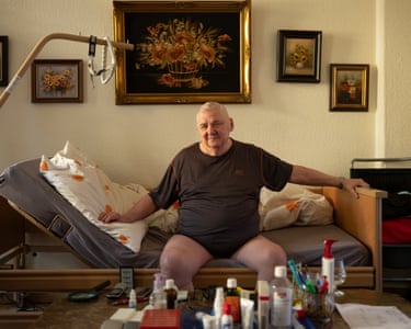 Günther Stanzl, 84, Berlin-Wilmersdorf, sitting in t-shirt and pants on his bed looking cheerfully towards the camera