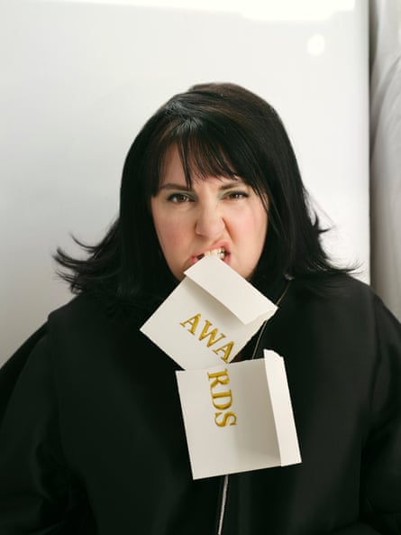 Portrait of Lenham Dunham wearing a black jacket and biting a torn-up envelope with ‘Awards’ written on it in gold
