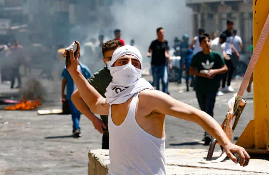 A Palestinian youth hurls rocks toward Israeli security forces, during confrontations with them in the occupied West Bank city of Hebron, on May 14, 2021. Photo by Hazem Bader/AFP