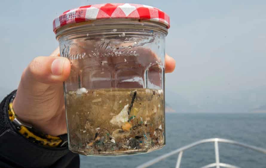 An environmental sciences student from the University of Hong Kong holds up a glass jar containing a sample of microplastics collected from the ocean.