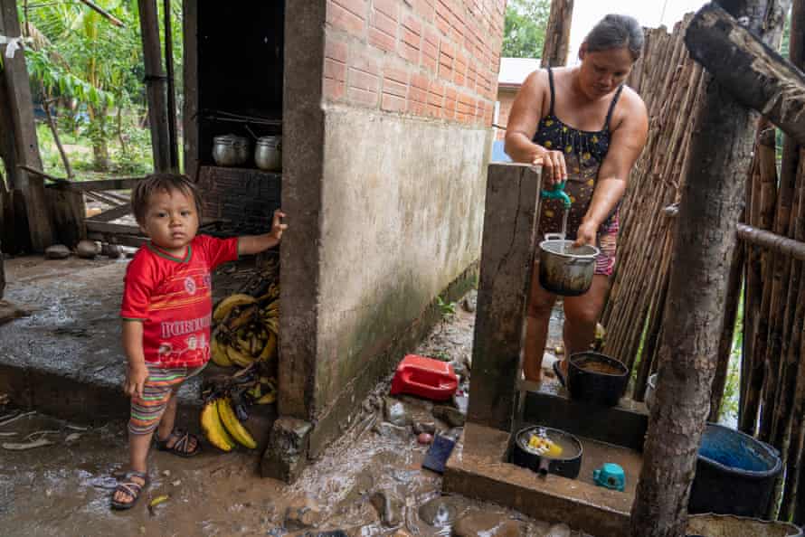 A woman fills a pot at an outside tap, while her son stands nearby