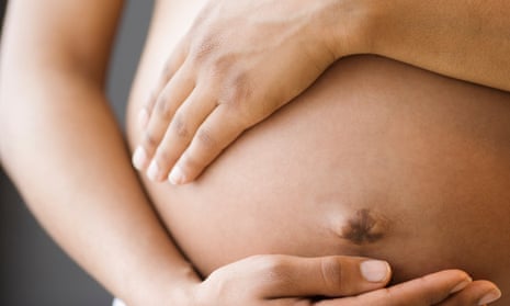 Stock close-up of Black woman's pregnant belly and hands holding it on the top and under the belly button.