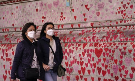 Two women wear a face mask while walking past the national Covid memorial wall, on the South Bank of the Thames in London.