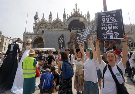 Protesters, two dressed as a bride and groom and others holding placards reading ‘we are the 99%, we hold the power’, gather in front of St Mark’s Basilica.