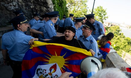 Hungarian police surround a man with a Tibetan flag on pathway with Budapest visible in the distance.