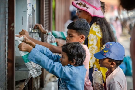 Three children and a woman fill water bottles from a tap on a street.