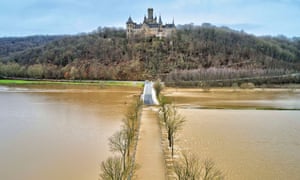 Flood water partially submerges a bridge across the river, with the castle on a hill behind