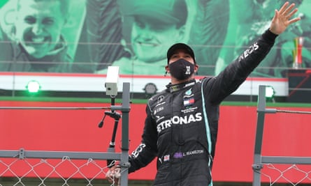 Lewis Hamilton waves to the spectators after winning the Portuguese Grand Prix, with the image of Michael Schumacher (top left) in the background.