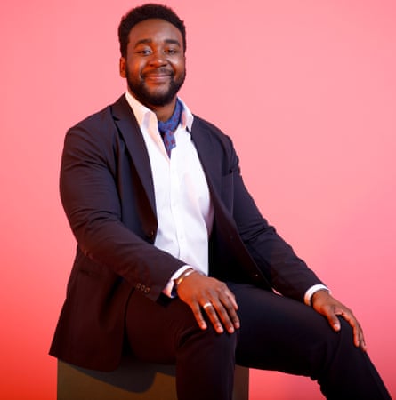 Kaf Okpattah sitting in a suit, open-necked shirt and neckerchief