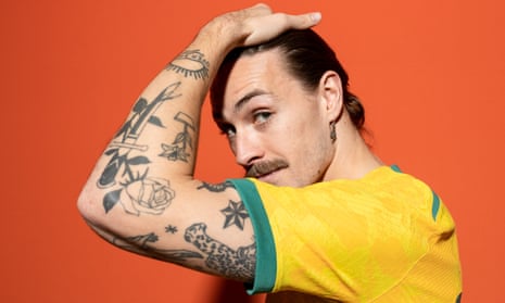 A portrait of Jackson Irvine in profile with his tattooed arm held up to his head