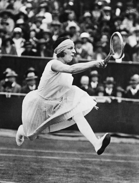 She reaches to hit a return while wearing a headscarf and long pleated skirt. The photograph is in black and white.