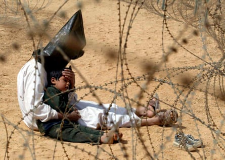 A hooded Iraqi man, seen through a wire fence, comforts his son at a prisoner of war camp in Najaf, Iraq, in 2003.