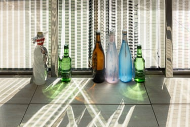 Lotus L. Kang’s artwork: seven glass bottles of different colours against a striped, sunlit window