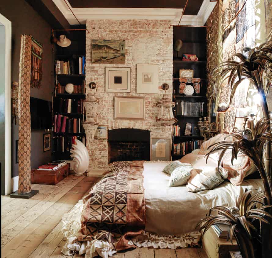 A bedroom with a whitewashed brick wall, a black wall and ceiling and a double bed with cushions and a blanket