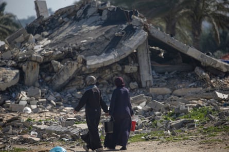 two women walk in front of a huge pile of rubble