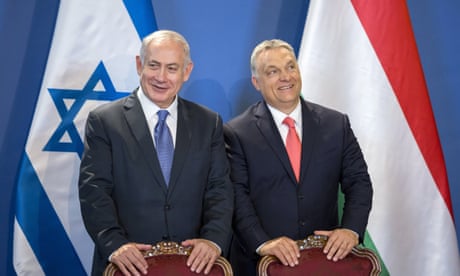 Benjamin Netanyahu and Viktor Orbán stand behind chairs in front of the flags of their respective countries