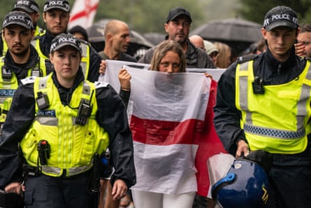 Protester holding an England flag to her face is flanked by police officers as she marches