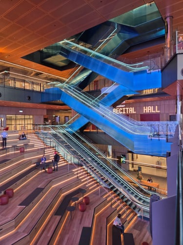 Crisscrossing blue escalators rise through ECU City’s atrium above tiered wooden seating steps