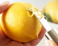 Closeup of a hand removing a lemon skin with a zesting knife