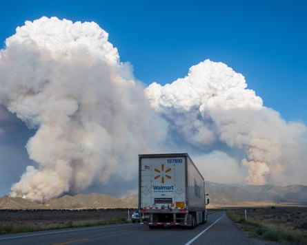A truck drives toward massive smoke plumes along a highway
