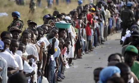 Residents of a tent city stand in line to receive food at an aid station in the Cite' Soleil