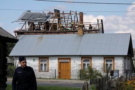 A police officer stands below as firefighters work on the destroyed roof of a house in Wyryki-Wola, Lublin Voivodeship, Poland
